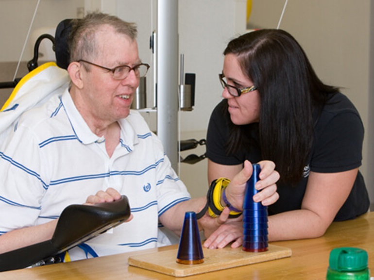 Patient and therapist engage in a rehabilitation exercise, stacking cones for coordination improvement.