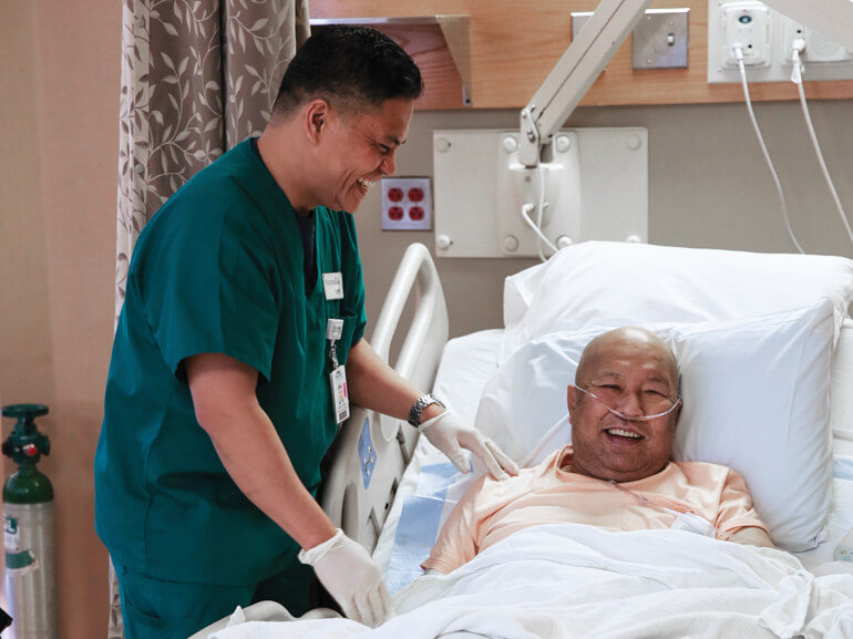 Therapist standing bedside with smiling rehabilitation patient
