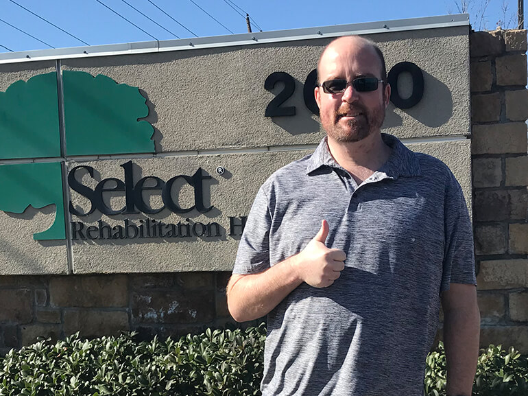 Jason giving thumbs-up in front of Select Rehabilitation Hospital sign.