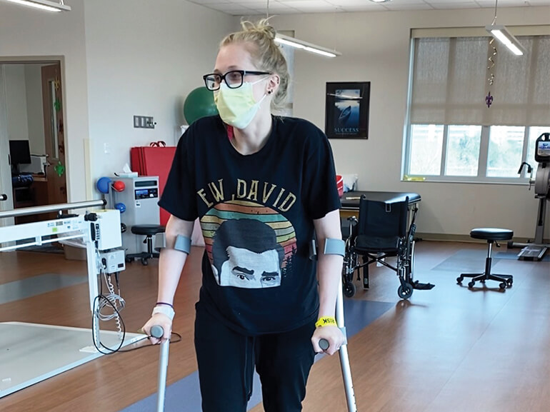Callie Clark progressing in her rehabilitation journey, diligently walking with crutches while wearing a face mask.