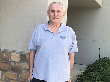 Dennis wearing gray polo shirt standing outside and smiling.