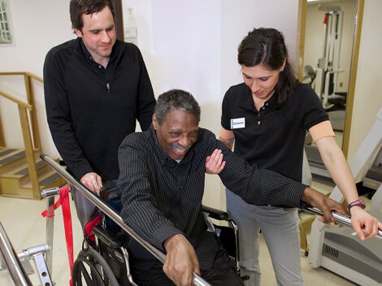 Patient in a wheelchair uses bars to help stand.