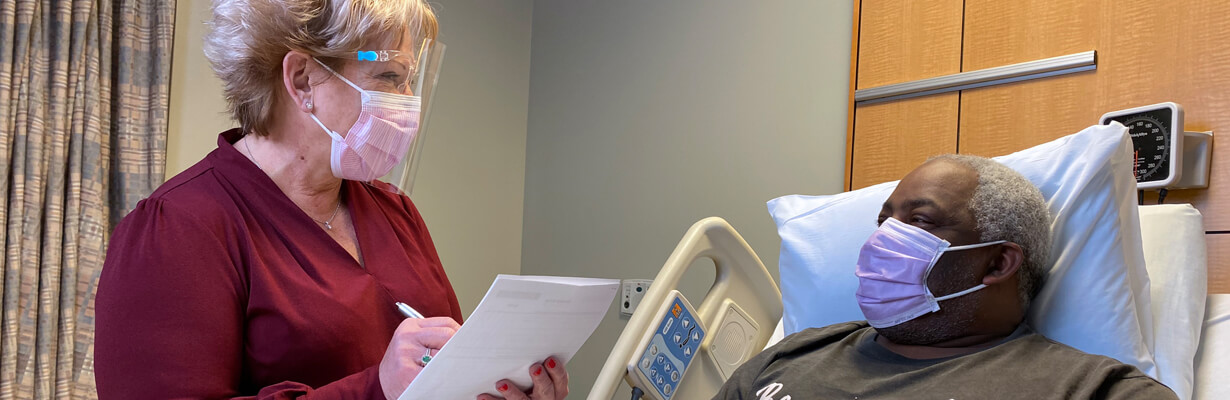 A healthcare professional discussing with a patient in a hospital setting, wearing personal protection with mask and shields.