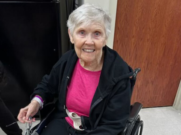 A woman sits in a wheelchair and smiles at the camera.